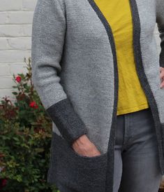 a woman standing in front of a brick wall wearing a gray and yellow cardigan