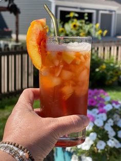 a person holding up a drink with an orange slice on the rim and ice in it