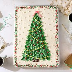 a decorated christmas tree cake sitting on top of a white table next to coffee cups