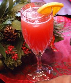 a drink in a wine glass on a table with pine cones and greenery around it