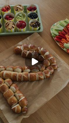 hot dogs wrapped in bread sitting on top of a wooden table next to trays of vegetables