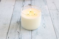 a lit candle sitting on top of a white wooden table next to a glass container