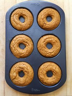 six doughnuts in a pan on a wooden table with one missing the middle