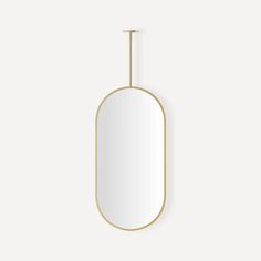 an oval mirror hanging on the wall with a gold frame and metal bar at the bottom