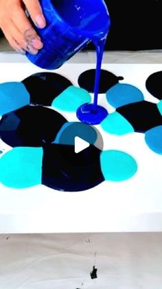 a person pouring blue liquid on top of black and white circles in the center of a table