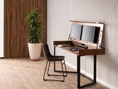 a desk with a computer on it next to a potted plant and a chair