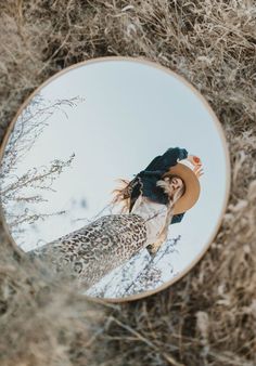 a mirror with a reflection of a woman wearing a cowboy hat in the middle of dry grass