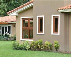 a brown house with two windows and plants in the front yard