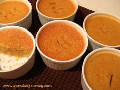 six white cups filled with food on top of a brown place mat in front of a counter