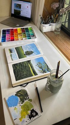 an open laptop computer sitting on top of a table next to art supplies and paint