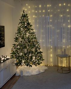 a living room with a christmas tree in the corner and lights on the wall behind it