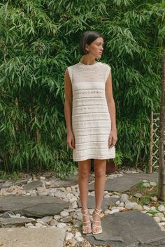 a woman standing in front of a bamboo tree wearing a white crochet dress