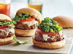 three hamburgers with lettuce, tomato and cheese on them sitting on a cutting board