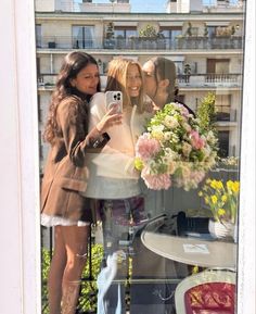 two women taking a selfie in front of a window with flowers and vases