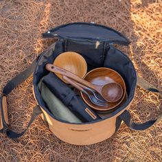 an open bag filled with wooden bowls and spoons on top of dry brown grass