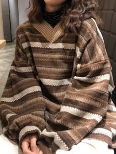 a woman is sitting down wearing a brown and white striped sweater