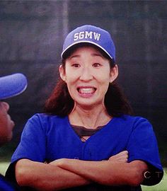 a woman in a baseball uniform with her arms crossed and smiling at another woman who is wearing a hat