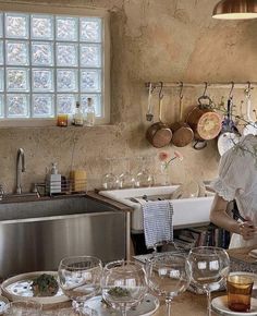 a woman standing in front of a kitchen counter filled with dishes and wineglasses