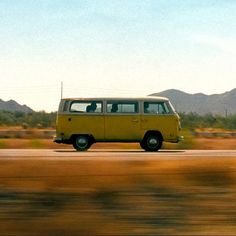 a yellow van is driving down the road in front of some mountains and desert grass