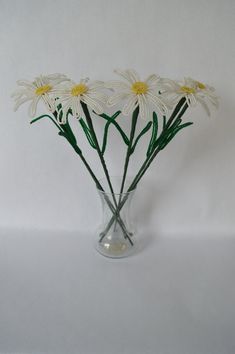 a clear vase filled with white daisies on top of a white table next to a wall