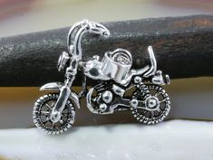 a close up of a silver motorcycle charm on a piece of wood with a branch in the background