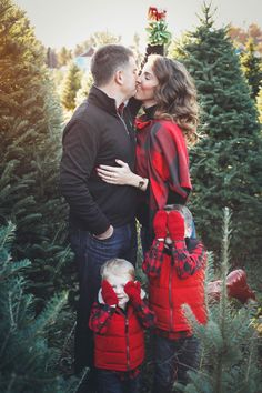 a man and woman kissing while standing in front of christmas trees with their little boy