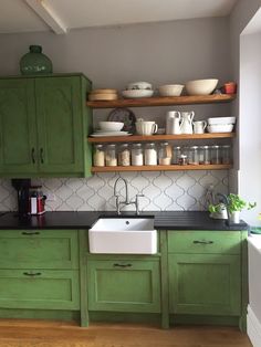 a kitchen with green cabinets and black counter tops, white tiles on the backsplash