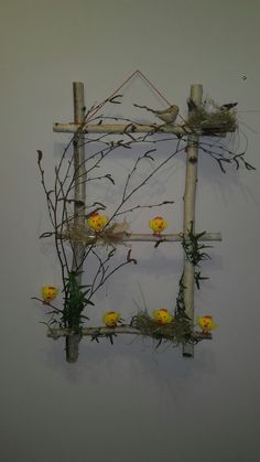 a sculpture made out of sticks and branches with flowers on it's sides, hanging from the wall