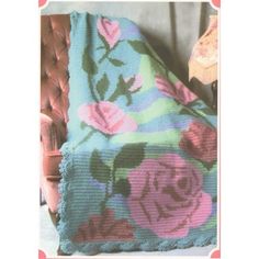 a crocheted blanket with pink roses on it and a brown chair in the background