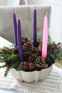 a white bowl filled with pine cones and purple candles