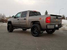 a silver truck parked in a parking lot with snow on the ground and trees behind it