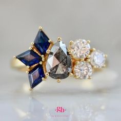 three different colored stones in an 18k yellow gold ring with diamonds on the sides