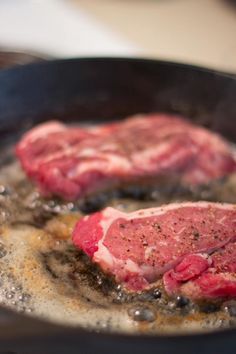 two steaks cooking in a skillet with sauce and pepper sprinkled on them