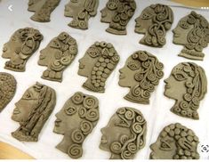 many clay heads are displayed on a table with white paper behind them and one is in the process of being carved