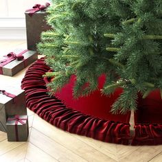 a christmas tree with presents under it on the floor next to a red round box