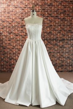 a white wedding dress is on display in front of a brick wall with a mannequin