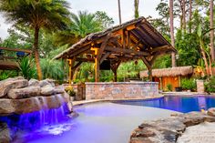 an outdoor pool with waterfall and gazebo surrounded by palm trees, rocks and water features