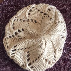 a white knitted hat sitting on top of a purple cloth covered floor next to a wooden table