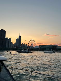 boats in the water near a large city at sunset with a ferris wheel in the background