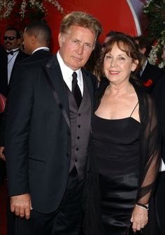 an older man and woman standing next to each other on a red carpet in formal wear