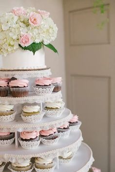 a tiered cake with cupcakes and flowers on top