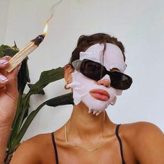 a woman with a mask on holding a matchstick in front of her face while wearing sunglasses