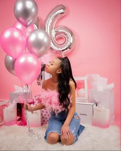 a woman sitting on the floor with balloons and presents in front of her, she is holding a number six balloon