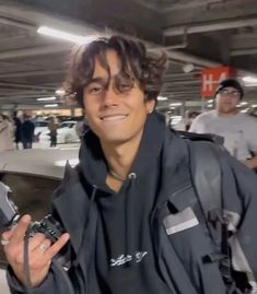 a man holding a camera in his right hand and smiling at the camera with other people behind him