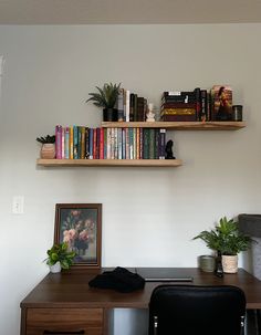 a wooden desk topped with lots of books next to a wall mounted shelf filled with plants