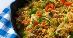 a pan filled with noodles and vegetables on top of a blue checkered table cloth