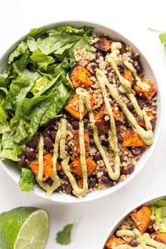 two white bowls filled with black beans, rice and lettuce next to lime wedges