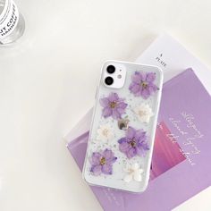 an iphone case with purple and white flowers on it next to a stack of books