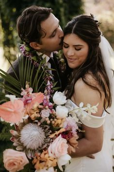 a bride and groom kissing each other in front of some trees with flowers on them