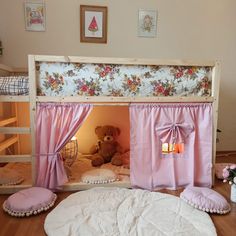 a teddy bear sitting in the corner of a bunk bed with pink curtains and pillows